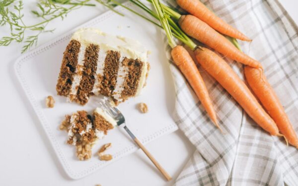 A slice of carrot cake with cream cheese frosting and fresh carrots beautifully arranged.