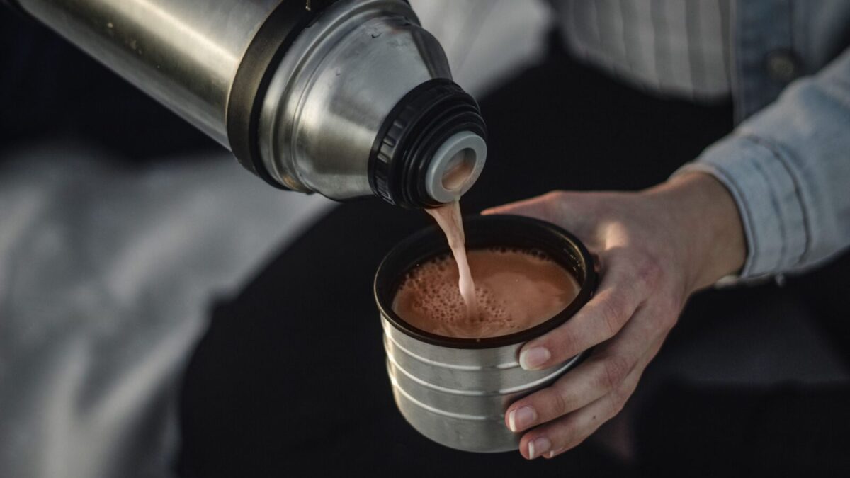 From above of crop anonymous female pouring aromatic hot coffee in thermos cap on blurred background