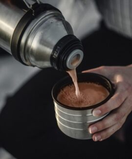 From above of crop anonymous female pouring aromatic hot coffee in thermos cap on blurred background