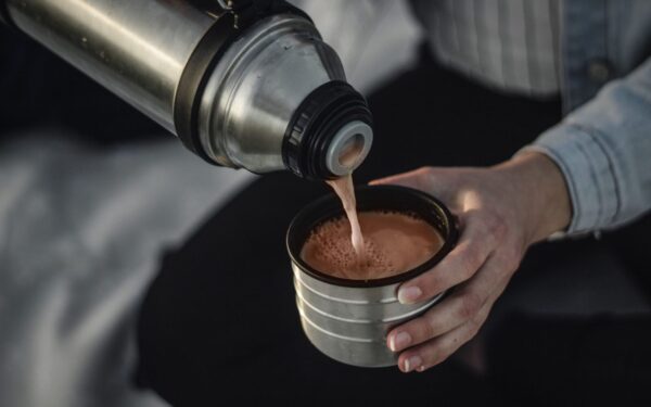From above of crop anonymous female pouring aromatic hot coffee in thermos cap on blurred background