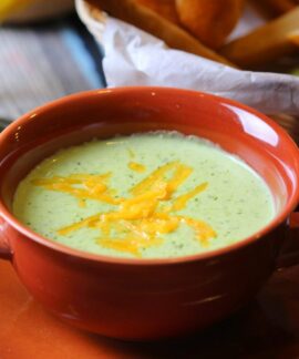 Close-up of creamy broccoli soup in a terracotta bowl with cheddar garnish.