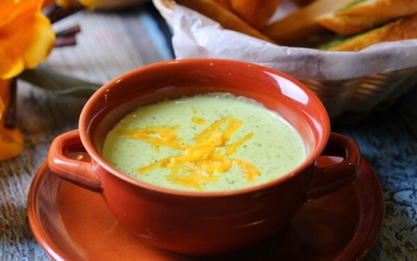 Close-up of creamy broccoli soup in a terracotta bowl with cheddar garnish.