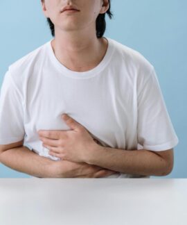 An adult man in a white shirt holds his stomach, indicating pain and discomfort, with a light blue background.