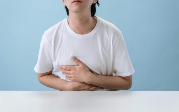 An adult man in a white shirt holds his stomach, indicating pain and discomfort, with a light blue background.
