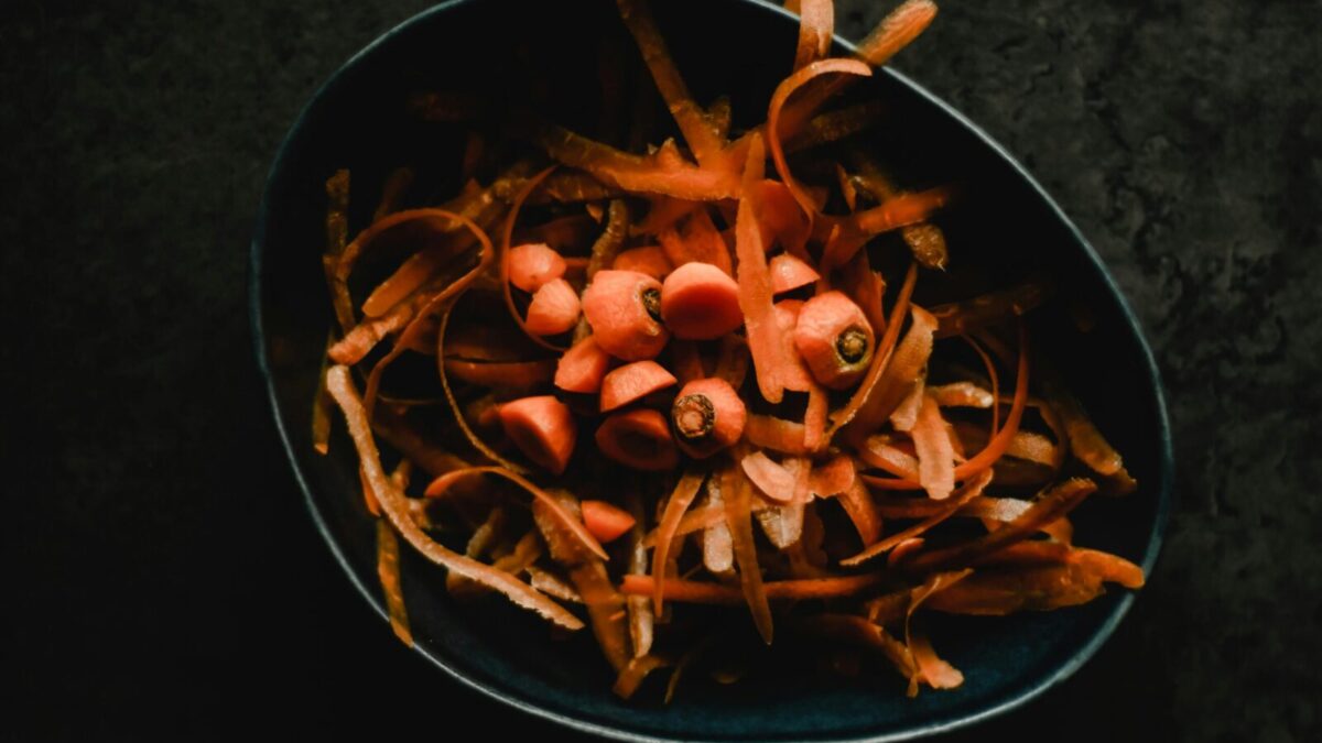 Close-up photo of fresh carrot peels and scraps in a dark bowl, perfect for food waste or preparation themes.