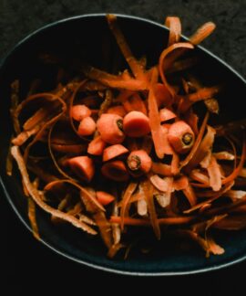Close-up photo of fresh carrot peels and scraps in a dark bowl, perfect for food waste or preparation themes.