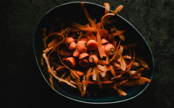 Close-up photo of fresh carrot peels and scraps in a dark bowl, perfect for food waste or preparation themes.