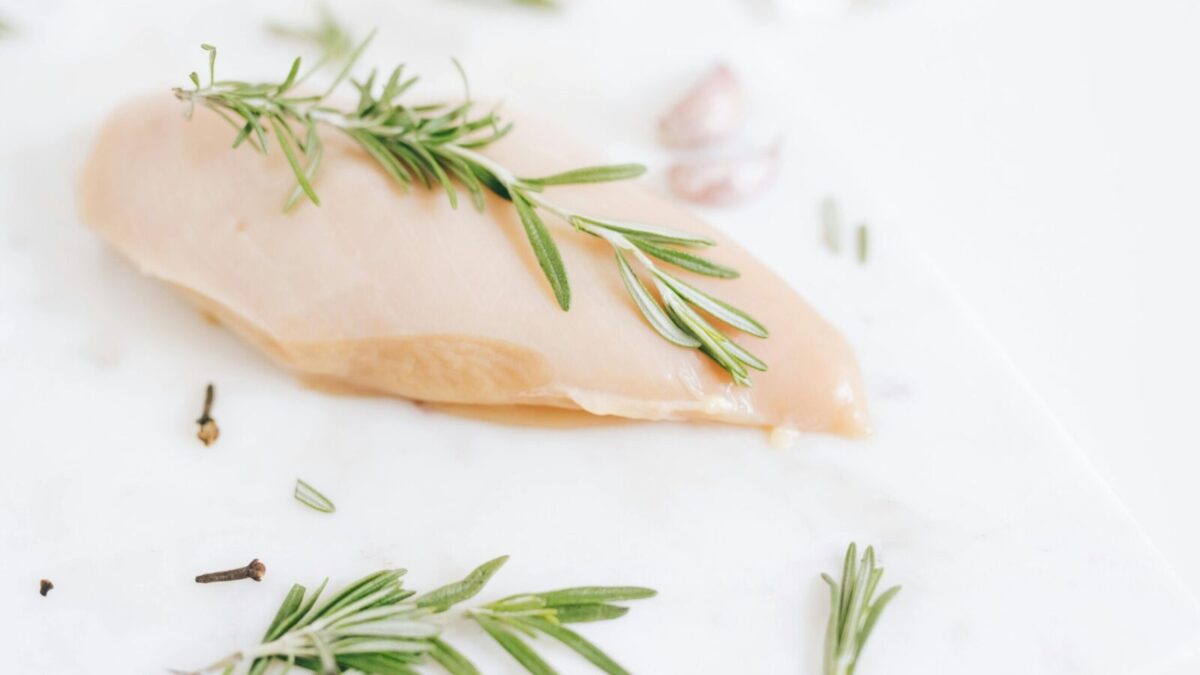Healthy raw chicken breast garnished with rosemary on a marble surface.