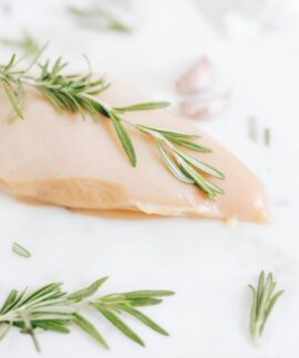 Healthy raw chicken breast garnished with rosemary on a marble surface.