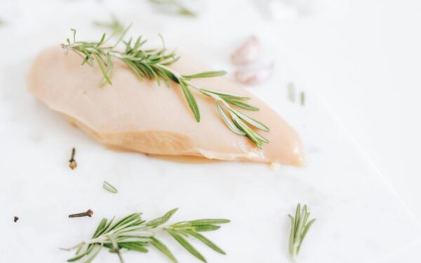Healthy raw chicken breast garnished with rosemary on a marble surface.