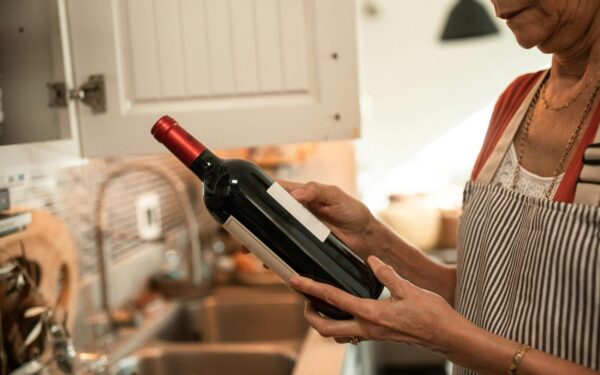 A senior woman examines a wine bottle in her cozy kitchen, wearing a striped apron.