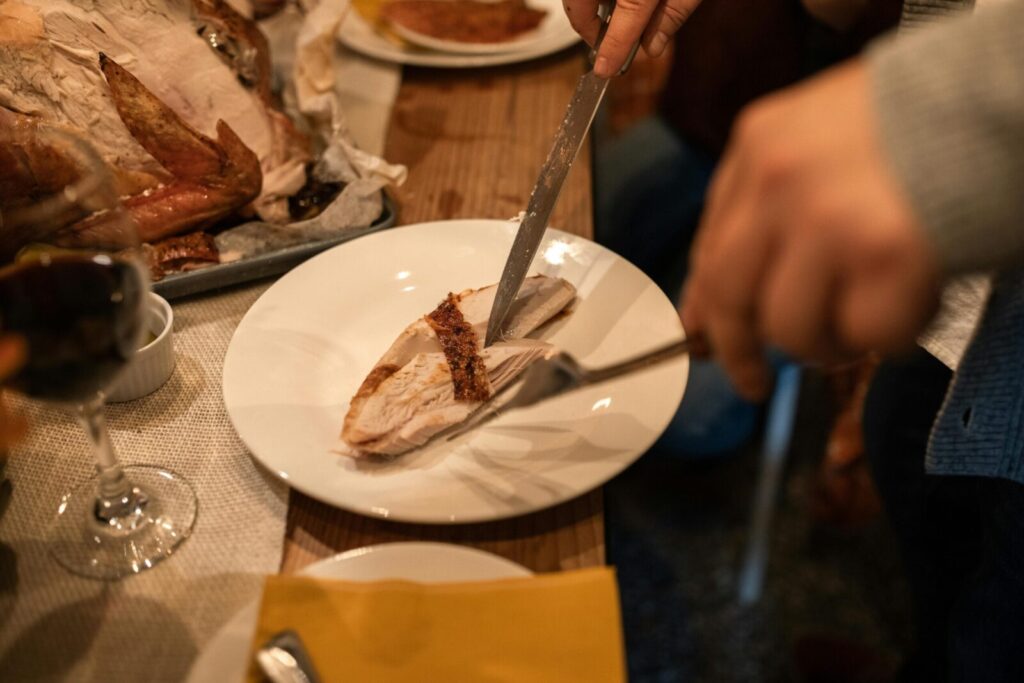 Close-up of slicing turkey breast at a Thanksgiving dinner with wine.