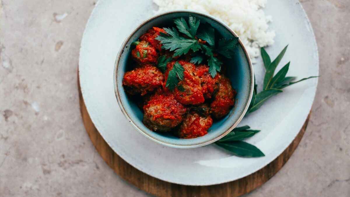 Top view of meatballs in tomato sauce served with rice, garnished with fresh herbs.