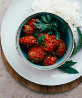 Top view of meatballs in tomato sauce served with rice, garnished with fresh herbs.