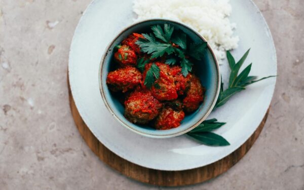 Top view of meatballs in tomato sauce served with rice, garnished with fresh herbs.