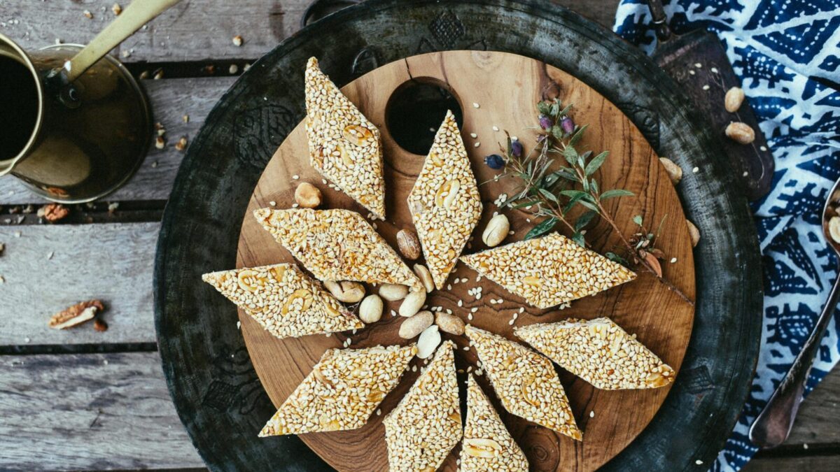 Close-up of diamond-shaped sesame seed and peanut brittle on a rustic wooden plate.