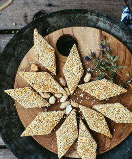 Close-up of diamond-shaped sesame seed and peanut brittle on a rustic wooden plate.