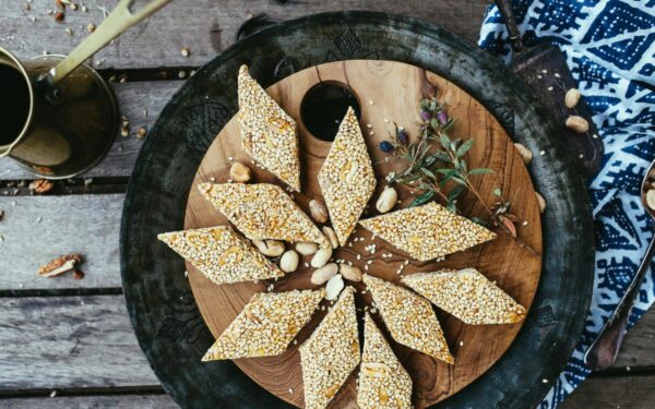 Close-up of diamond-shaped sesame seed and peanut brittle on a rustic wooden plate.
