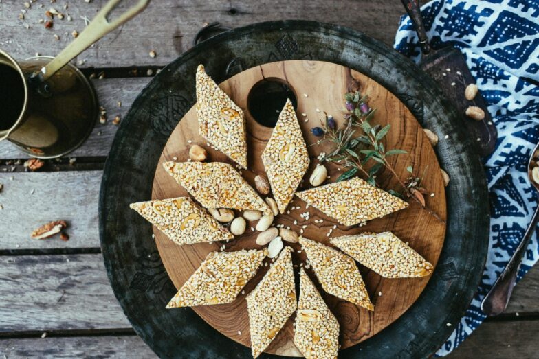 Close-up of diamond-shaped sesame seed and peanut brittle on a rustic wooden plate.