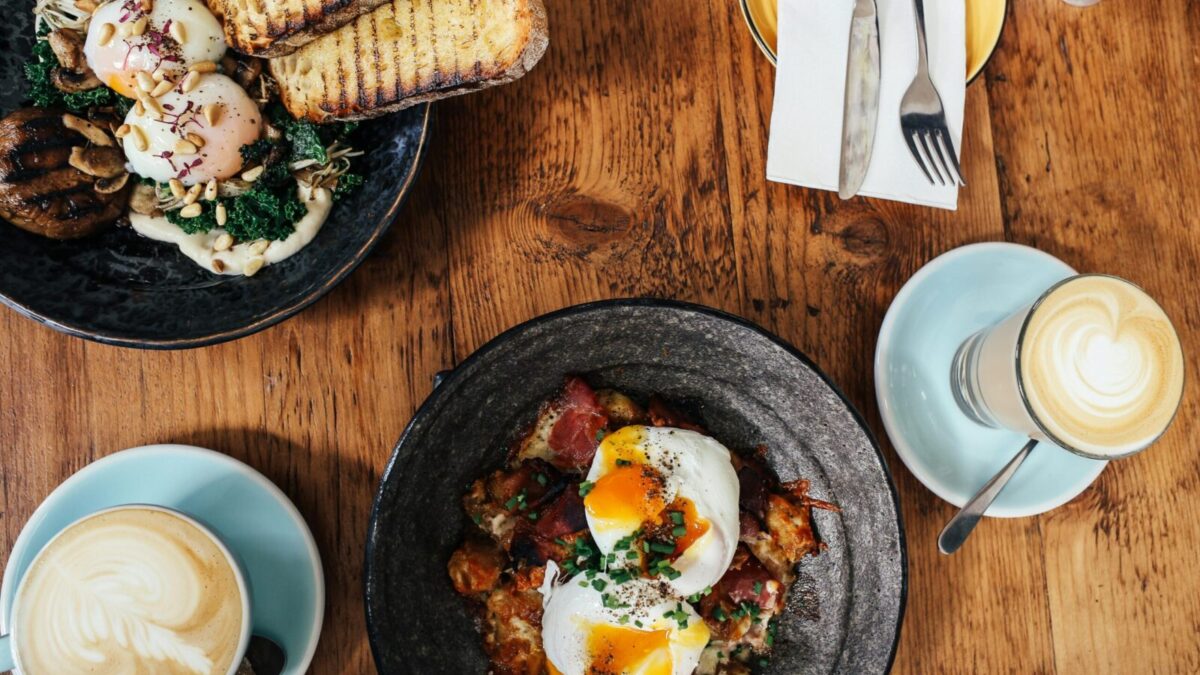 Top view of a delightful brunch spread featuring poached eggs and lattes on a wooden table.