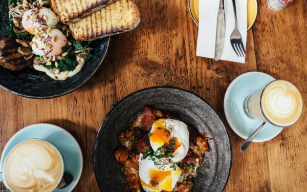 Top view of a delightful brunch spread featuring poached eggs and lattes on a wooden table.