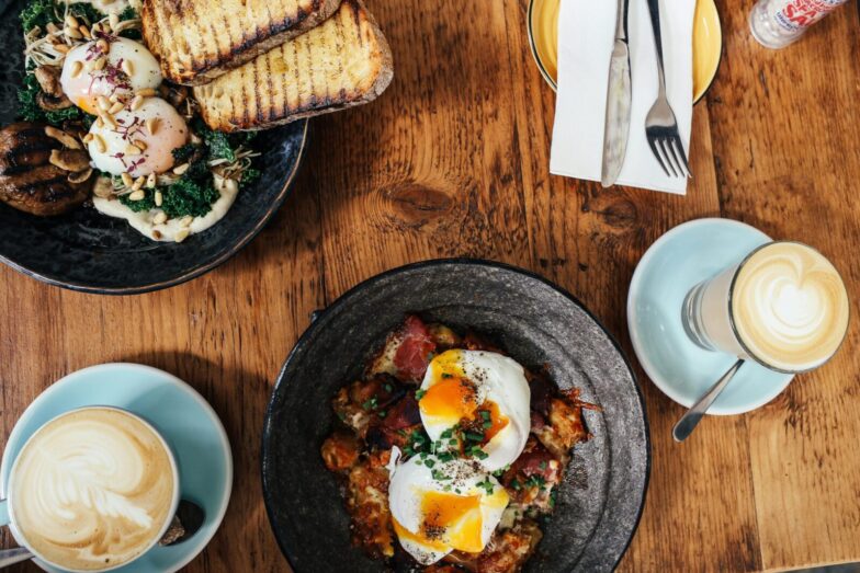 Top view of a delightful brunch spread featuring poached eggs and lattes on a wooden table.