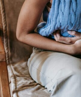 Crop unrecognizable female touching belly while having acute pain in stomach sitting on couch