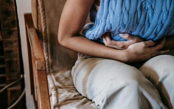 Crop unrecognizable female touching belly while having acute pain in stomach sitting on couch