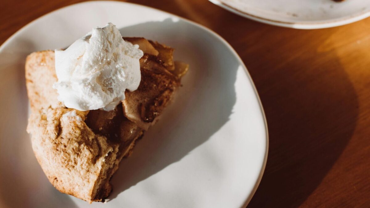 Close-up of a slice of homemade apple pie topped with whipped cream on a ceramic plate.
