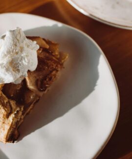 Close-up of a slice of homemade apple pie topped with whipped cream on a ceramic plate.
