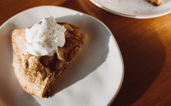 Close-up of a slice of homemade apple pie topped with whipped cream on a ceramic plate.