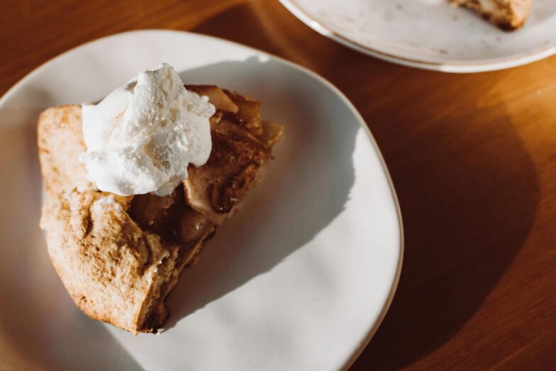 Close-up of a slice of homemade apple pie topped with whipped cream on a ceramic plate.