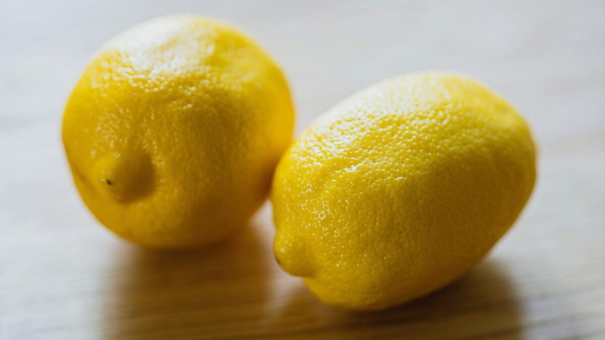 Ripe sour whole lemons placed on wooden surface in light room in kitchen with sunlight at home during harvest season