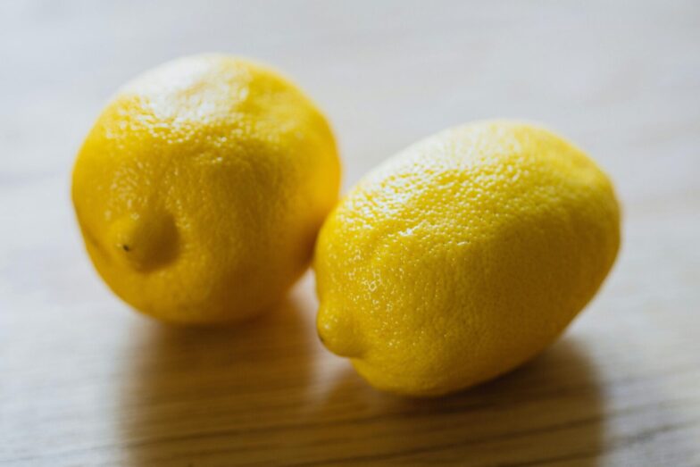 Ripe sour whole lemons placed on wooden surface in light room in kitchen with sunlight at home during harvest season