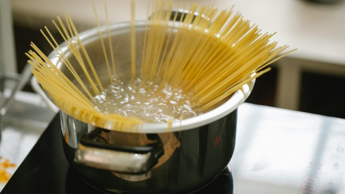 Raw spaghetti cooked in boiling water in saucepan placed on stove in light kitchen