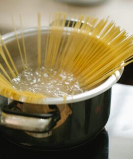 Raw spaghetti cooked in boiling water in saucepan placed on stove in light kitchen