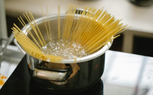 Raw spaghetti cooked in boiling water in saucepan placed on stove in light kitchen