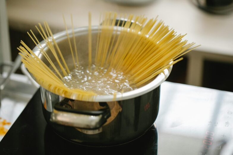Raw spaghetti cooked in boiling water in saucepan placed on stove in light kitchen