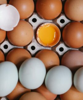 Top view of yolk in broken eggshell among whole eggs in carton container