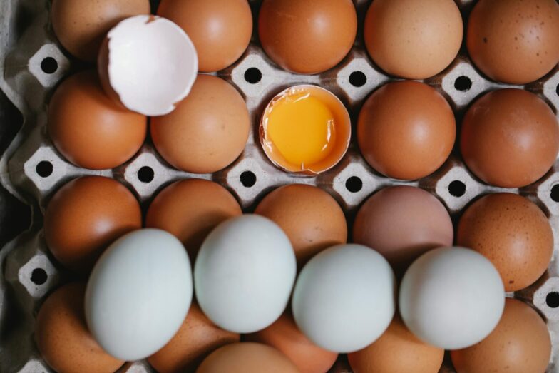 Top view of yolk in broken eggshell among whole eggs in carton container