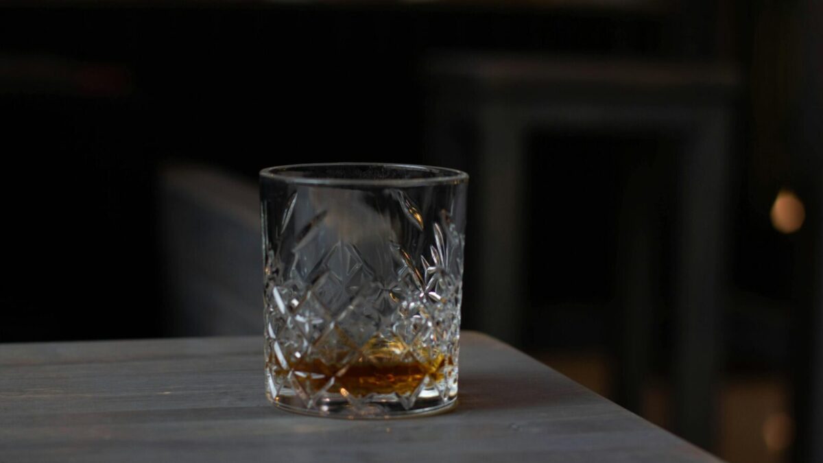 Cut glass with aromatic cognac on bottom placed on wooden table in dark living room