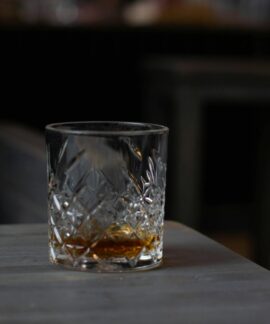 Cut glass with aromatic cognac on bottom placed on wooden table in dark living room