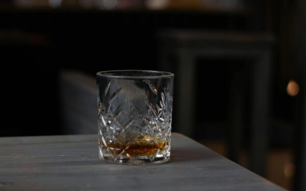 Cut glass with aromatic cognac on bottom placed on wooden table in dark living room