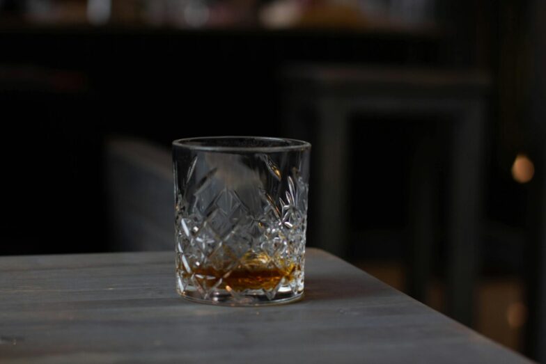 Cut glass with aromatic cognac on bottom placed on wooden table in dark living room