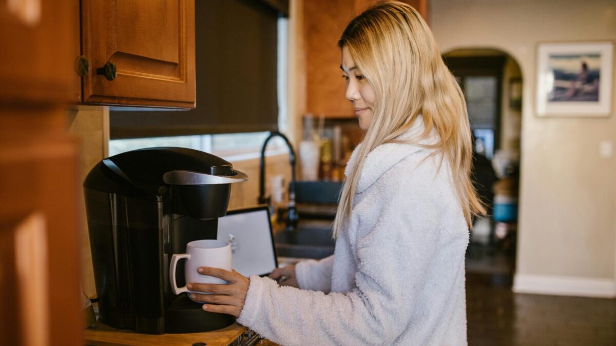 Woman with blonde hair making coffee in a cozy home kitchen setting.