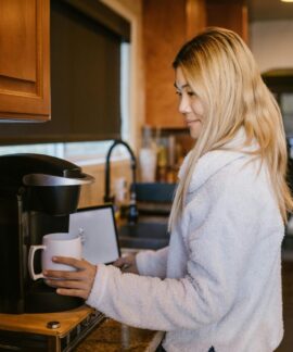 Woman with blonde hair making coffee in a cozy home kitchen setting.