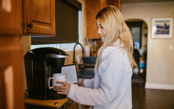 Woman with blonde hair making coffee in a cozy home kitchen setting.