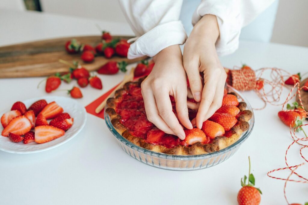 Hands arranging fresh strawberries on a pie, showcasing delicious homemade food preparation.
