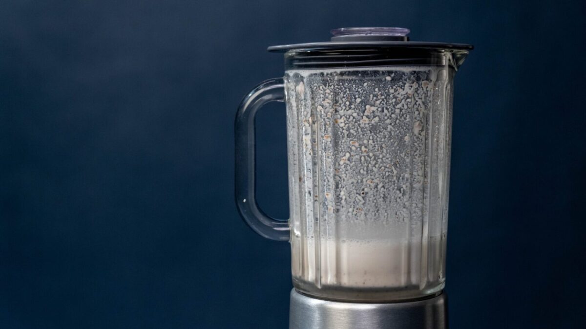 Close-up of a silver blender making a milkshake against a blue background, studio shot.