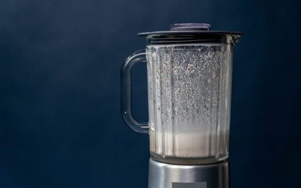 Close-up of a silver blender making a milkshake against a blue background, studio shot.